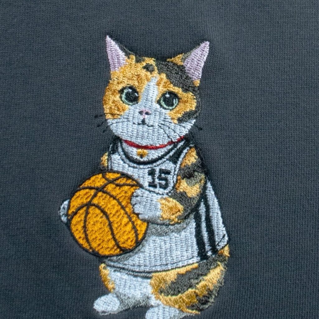 グレーのスウェットに直接刺繍したバスケットボールを持つ三毛猫